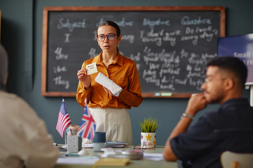 Teacher at a blackboard covered in grammar rules explaining English to adult students